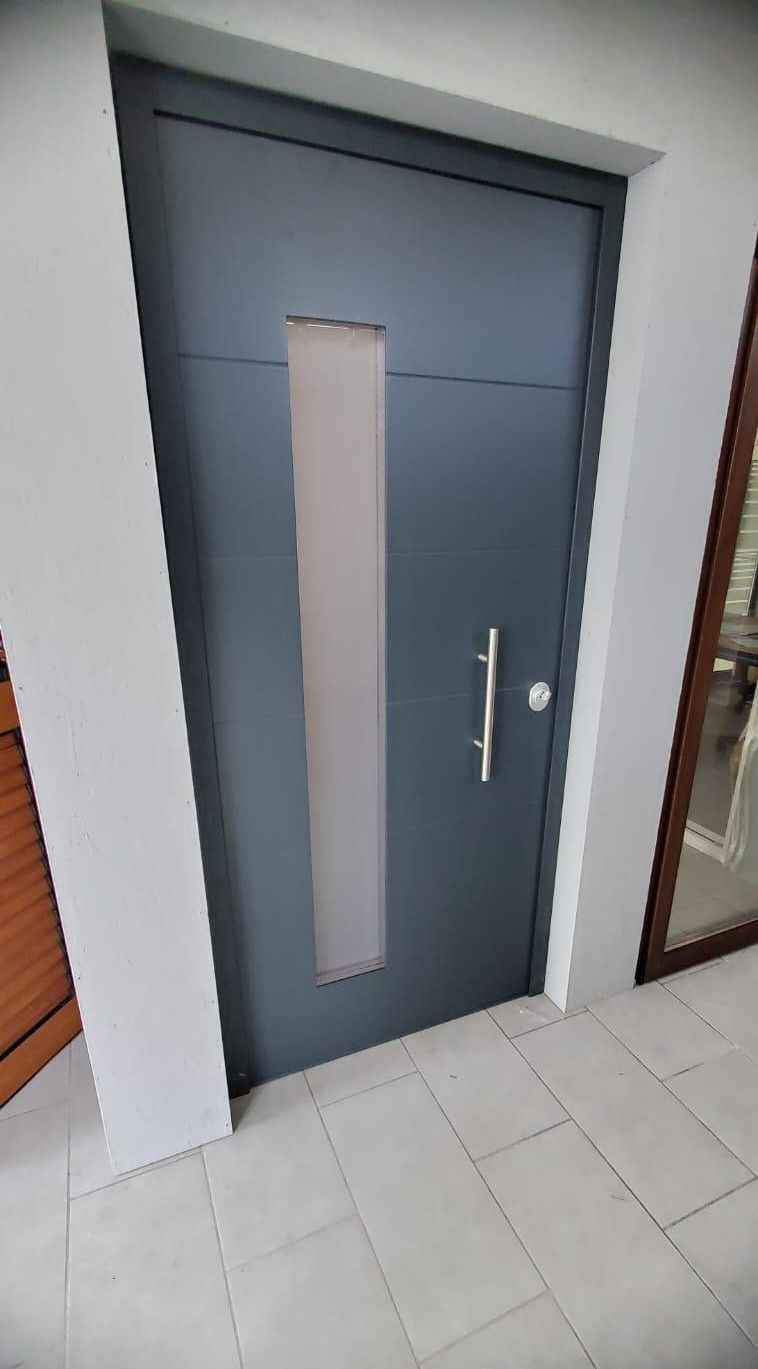 Portoncino d’ingresso grigio antracite con vetro verticale e maniglione, sotto un portico